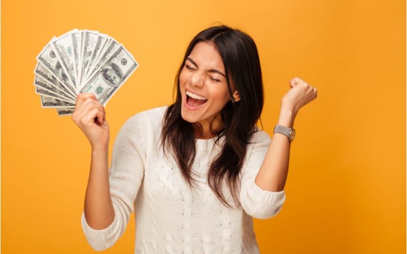 Portrait of a cheerful young woman holding money banknotes and celebrating isolated over yellow background because she found a cheap haircut near her