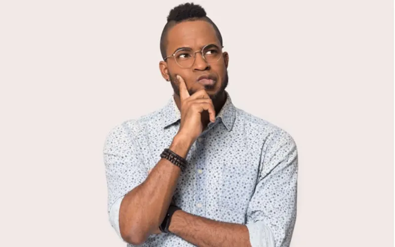 Thoughtful african guy thinking try solve problem pose isolated on grey studio background, worried black man in glasses feels concerned puzzled lost in thoughts pondering making decision concept image as an image for a piece on cheap haircuts near me