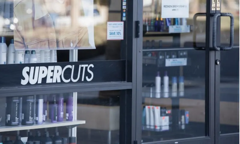 As an image for a piece on cheap haircuts near me, an exterior of a supercuts showing a door, the sign, and some of the products sold inside