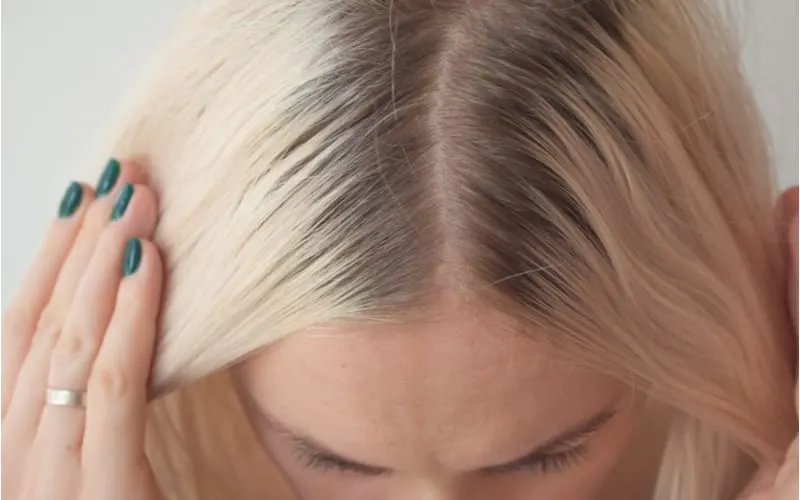 For a piece on hair extensions maintenance and cost, Closeup of a woman's blond head with parted hair regrown roots. Haircare, making new hairdo, hair therapy concept