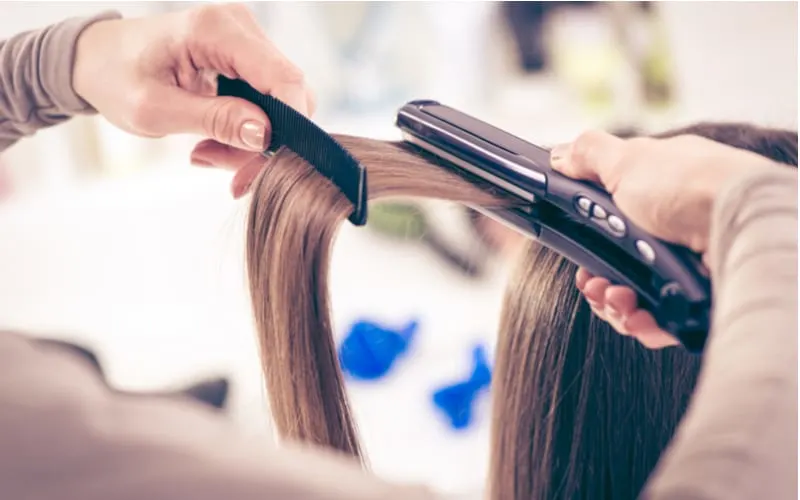 Close-up of a hairdresser straightening long brown hair with hair irons as an image for a piece on hair straightening cost