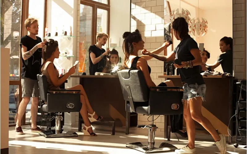 As an image for a piece on what is a hair salon, Picture of working day inside the beauty- sit on two chairs clients beautiful young girls. Hairdresser makes hair styling or hair cut, make-up artist doing make-up in a beauty salon- stock photo.