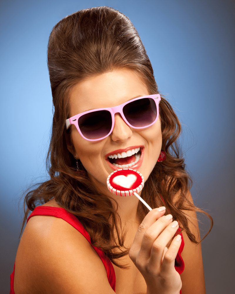 Laughing woman with a lollipop smiles and wears pink sunglasses with a bad haircut