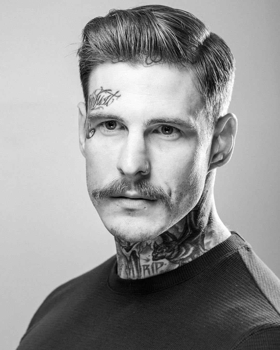 Guy with a peaky blinders haircut and face and neck tattoos
