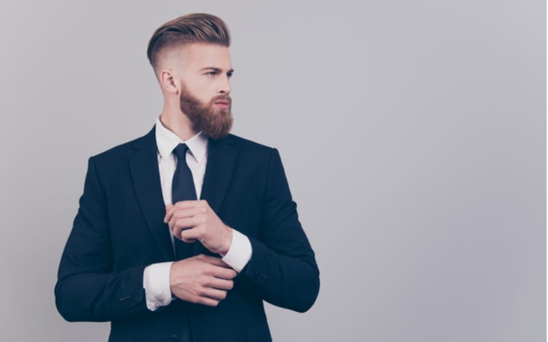 Man in a suit holding his sleeves and looking to his left with a high fade haircut
