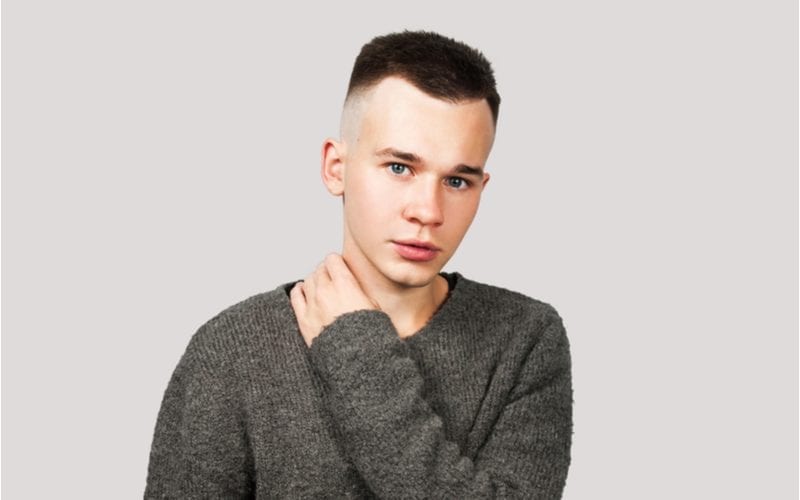 Portrait of white yong guy in gray sweater and short haircut, isolated on gray background.