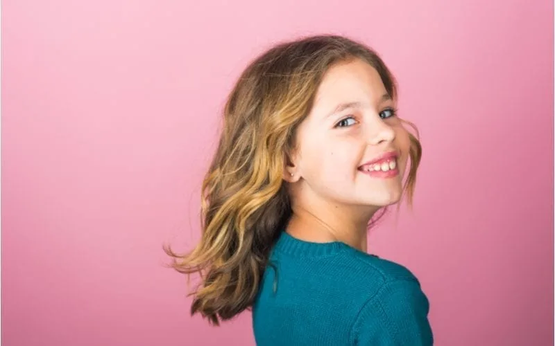 Little girl haircuts featuring a young gal smiling at the camera in front of a pink background