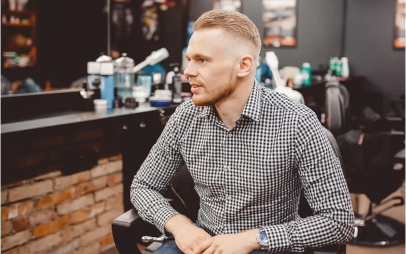 Man in barber chair, hairdresser styling in barbershop and rocking a high fade haircut