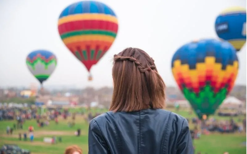 Woman with a short lob haircut standing away from the camera and looking at hot air balloons with braided short hair