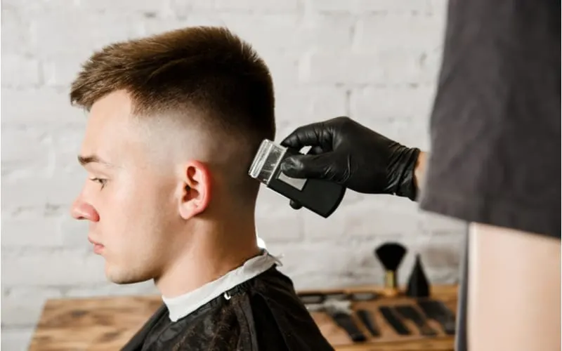 Barber hand in gloves cut hair and shaves young man on a brick wall background. Close up portrait of a guy with a teen boy haircut