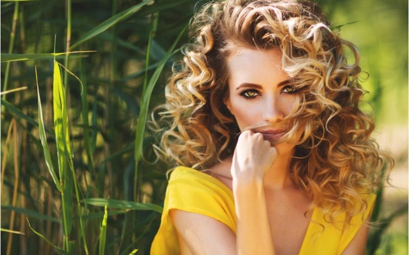 Summer fashion close up portrait of stunning blonde woman on the beach. Wearing long yellow dress with a curly haircut