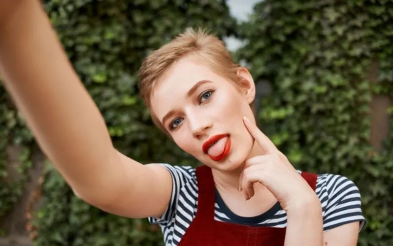 Woman wearing red lip and a pixie cut sticking her tongue out