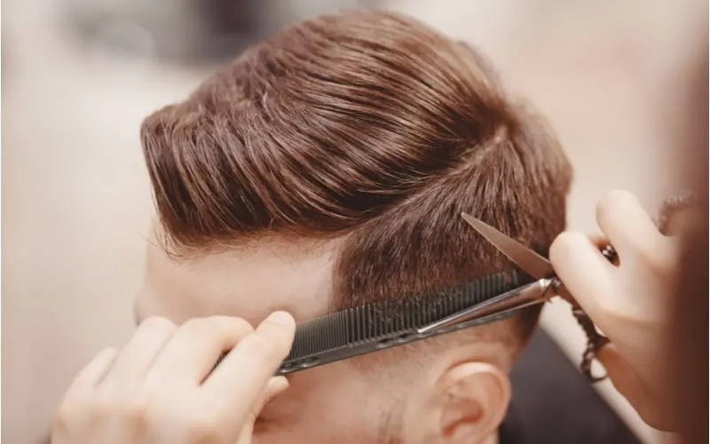 Close-up, master hairdresser does hairstyle with scissors comb