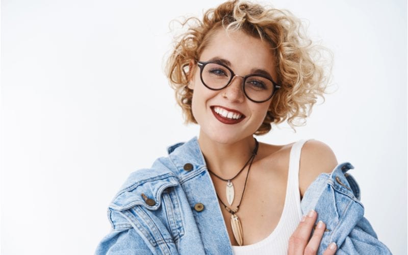 Happy delighted and attractive blond female with short curly hairstyle freckles and pierced nose wearing lipstick smiling joyfully tilting head relaxed and friendly looking at camera pleased