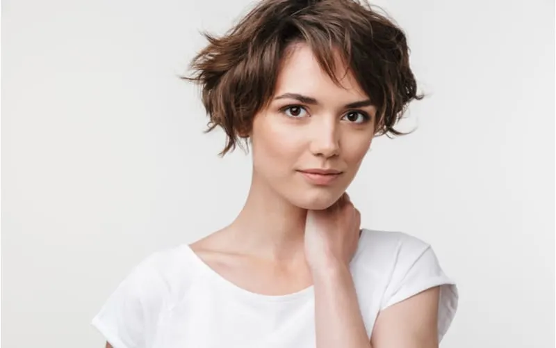 Portrait of young woman with short brown hair in basic t-shirt looking at camera while standing isolated over white background