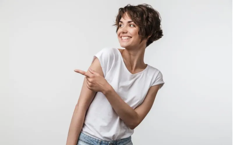 Portrait of happy woman with short shag hair in basic t-shirt rejoicing and pointing finger at copyspace isolated over white background