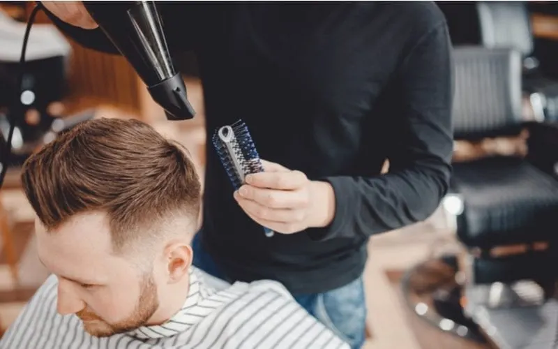 Close-up master Barber does hairstyle and styling with dryer hair to guy for a piece on the best hairstyles for balding men