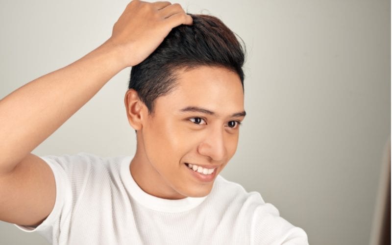 Man with a two block hairstyle holds his head and smiles in happiness