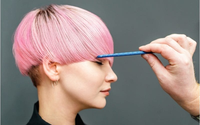 Woman with a two block haircut that is pink in color gets her hair combed by a blue comb