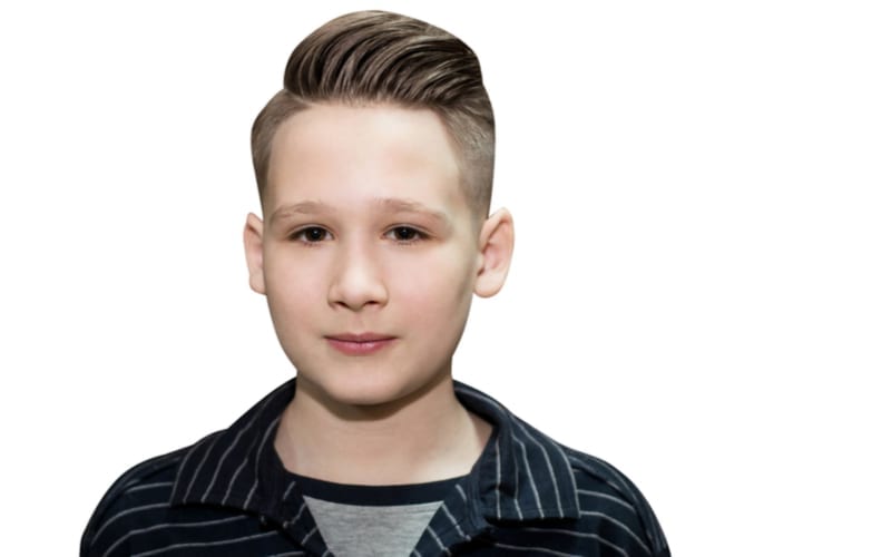Stylish modern retro haircut side part with mid fade undercut with parting of a schoolboy guy in a barbershop on isolated white background