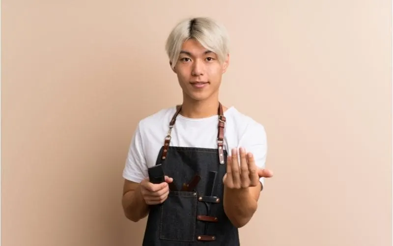 Young asian man with blonde dyed hair holds electronic shaver and motions 