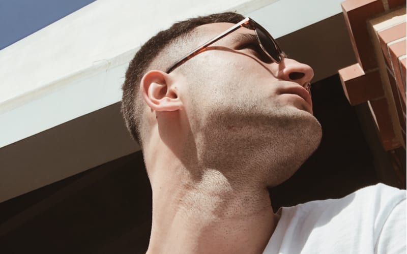 Selfie of a stylish and attractive man in profile wearing a white t-shirt and sunglasses. Handsome young man with shades and stubble looking aside under sunlight. Boy with trendy fade undercut haircut