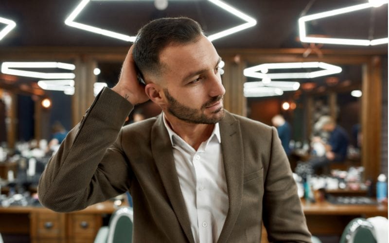 Handsome bearded man at barbershop. Portrait of stylish young guy in jacket touching his hair while visiting barbershop or salon