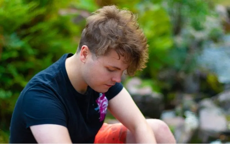 Man with an undercut two block hairstyle looks down at the ground while sitting outside