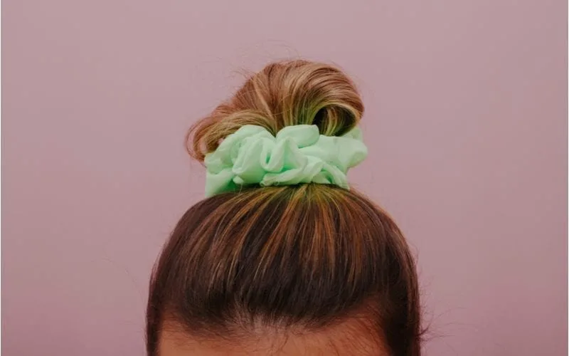 Unprofessional hairstyle in a scrunchie on top of her head on pink background