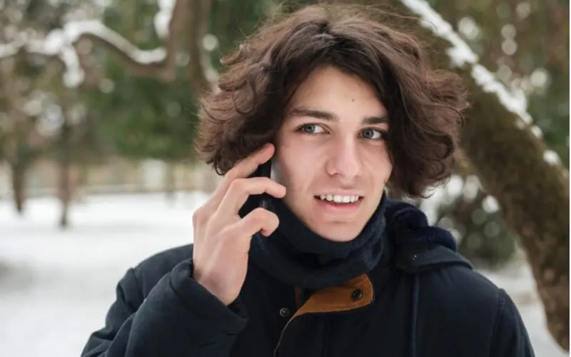As an image for a piece on teen boy haircuts, Portrait of a teenage boy with long hair in winter against the backdrop of snow-covered trees in the park