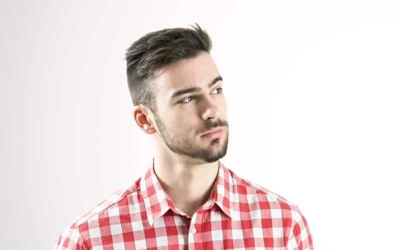 Portrait of serious young man in plaid shirt looking away over gray background for a piece on undercut haircuts