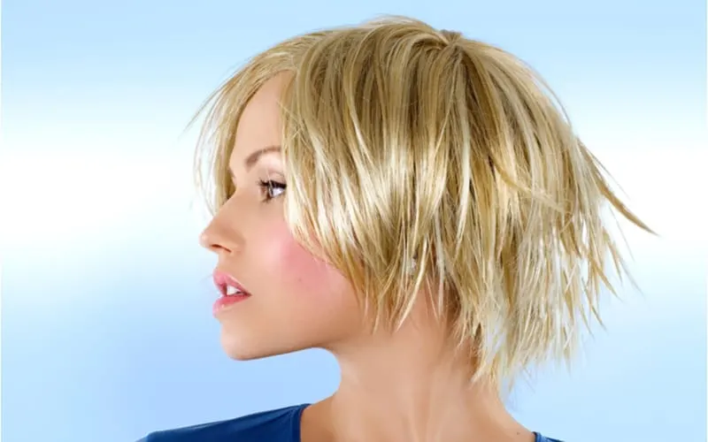 Blond model in studio rocking a short shag haircut and blue shirt against a light sky blue background
