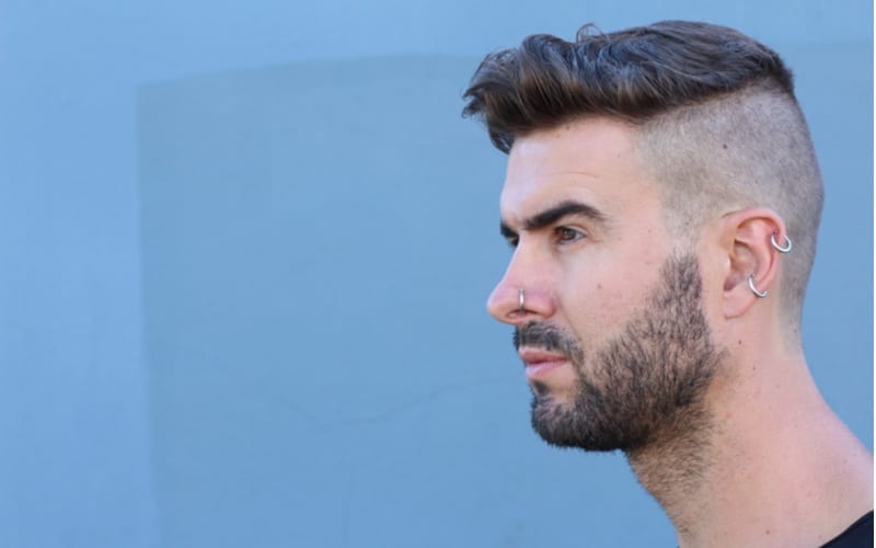 Profile view of handsome stylish young man with undercut hairstyle, beard and piercings with copy space
