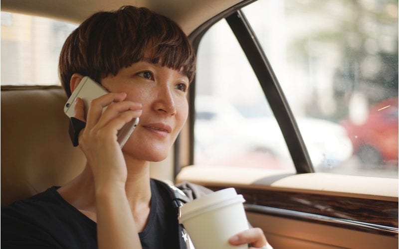 Asian woman with a two-block haircut holds a coffee and looks ahead in the cab in which she is riding