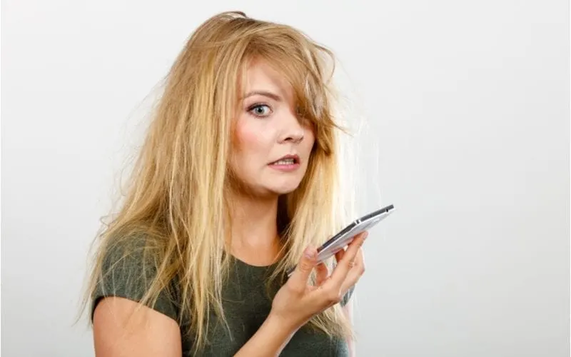 Person with an unprofessional hairstyle holds up a mobile phone to her face