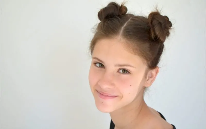 Woman looks directly at the camera wearing space buns against a grey background