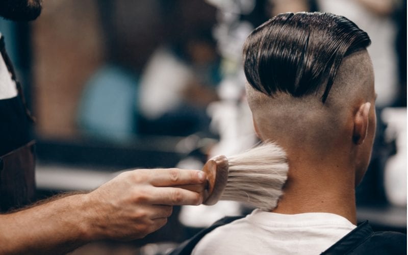 Close-up of a young hipster guy in a barber shop hairdresser shakes his hair, does talc. Concept men's place, toned photo