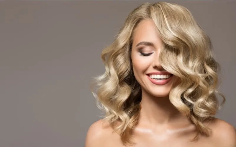 Blonde woman with curly beautiful hair smiling on gray background for a piece on curly haircuts