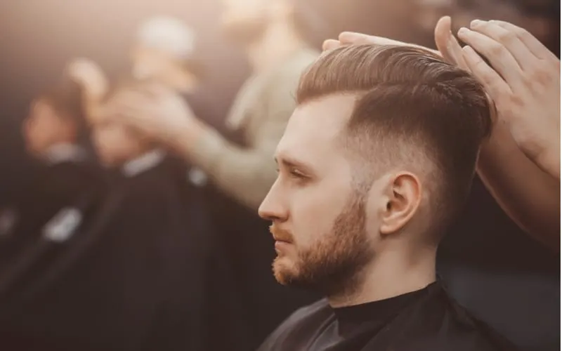 Man with a beard and a short side long top haircut getting styled by his barber