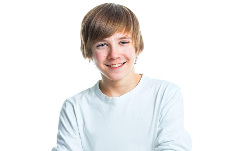 As an image for a piece on teenage boy haircuts, Close up portrait of young smiling cute teenager in white, isolated on white