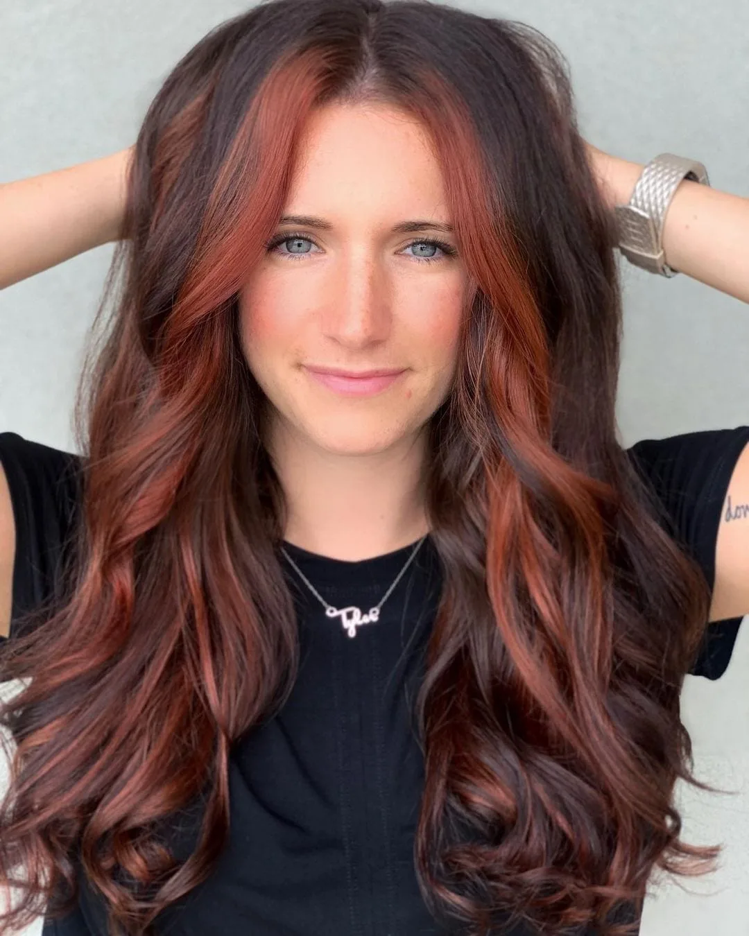 Woman with long, wavy ombre hair stands with her hands on her head