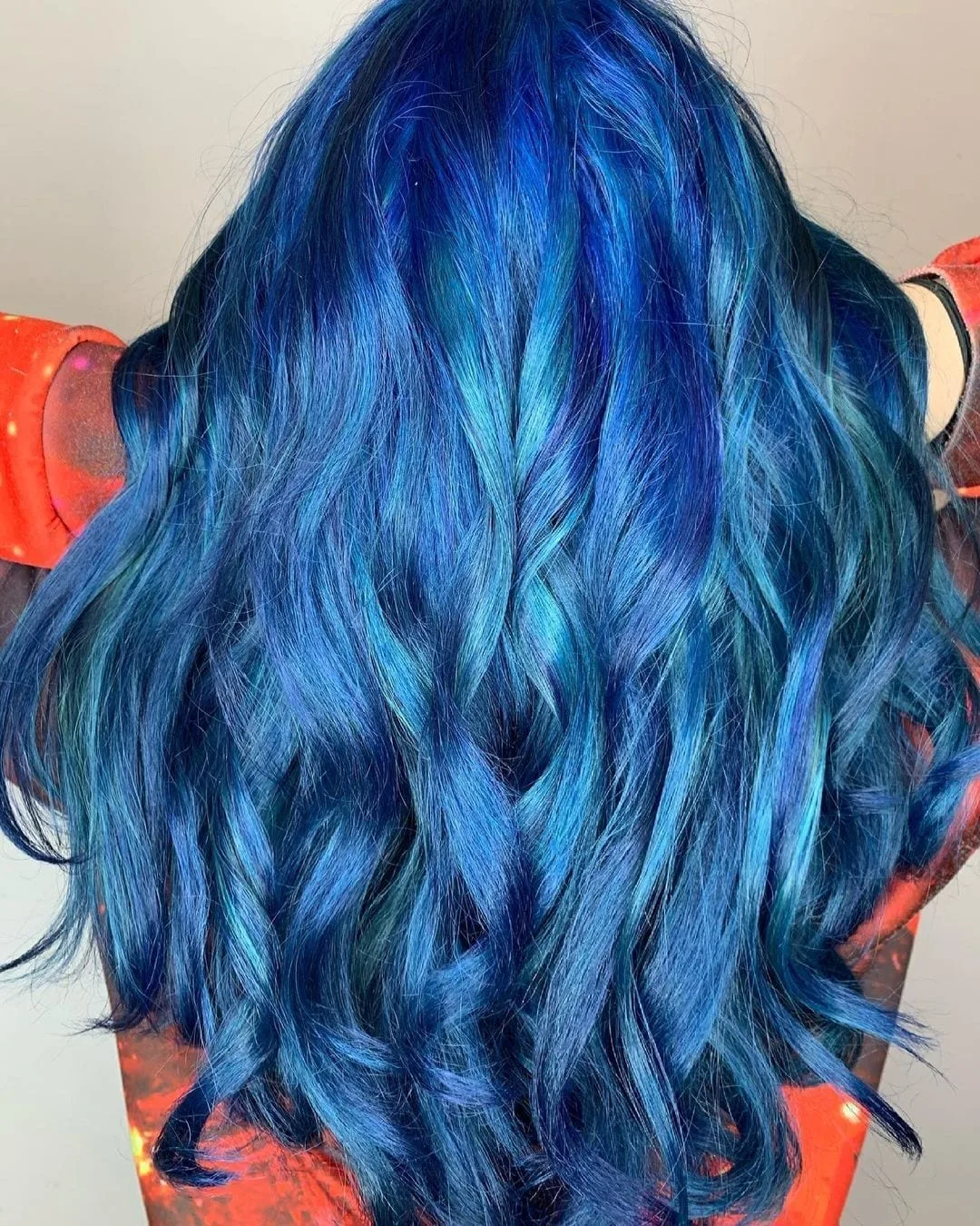 Woman with blue hair holds her hands on the top of her head
