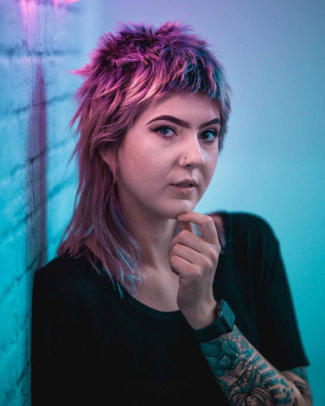Woman with a mullet that is colored with a faded galaxy haircut holds her chin