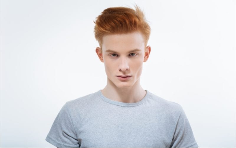 Man with a red headed hairstyle looks intensely at the camera and wears a tight grey tshirt