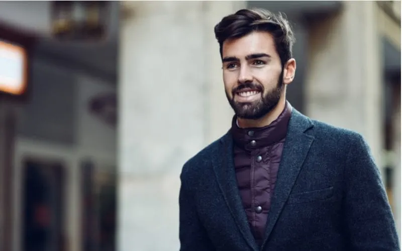 As an image for a piece on a haircut for guys with big foreheads, a man wears a British looking shirt and wool jacket while smiling and walking outside