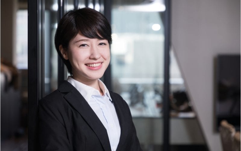Short hair asian woman smiles and wears a black suit with a white shirt