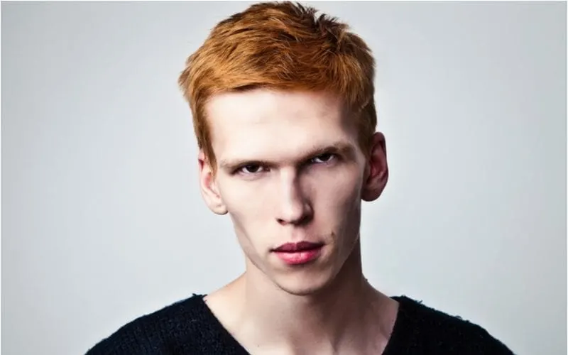 Young man with a red headed hairstyle and a pale complexion wears a ratty shirt and does not smile