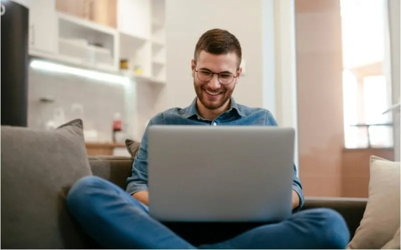 Man on his laptop with his legs crossed wears glasses and laughs