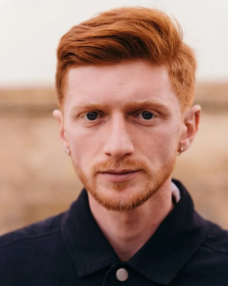 Young man with a red headed hairstyle and a buttoned up shirt standing in a field
