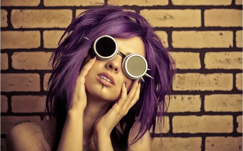 Punk girl with a lower lip stud and spikey sunglasses tilts her head to the left and holds her face